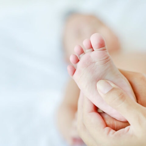 An infant's small foot cradled in an parents hands being massaged to increase parent-baby bonding.