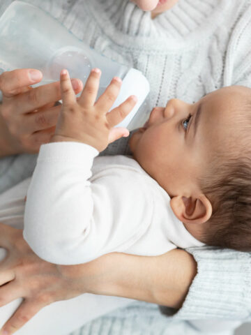 A close-up of a baby being lovingly fed by bottle in the secure hold a Newborn Care Specialist in Tampa, Florida