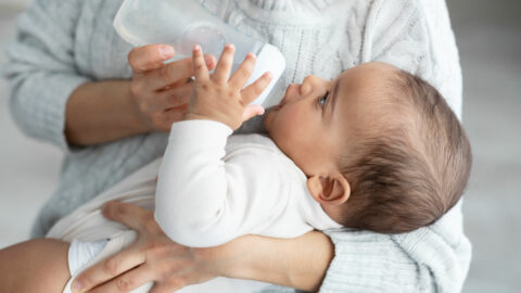 A close-up of a baby being lovingly fed by bottle in the secure hold a Newborn Care Specialist in Tampa, Florida
