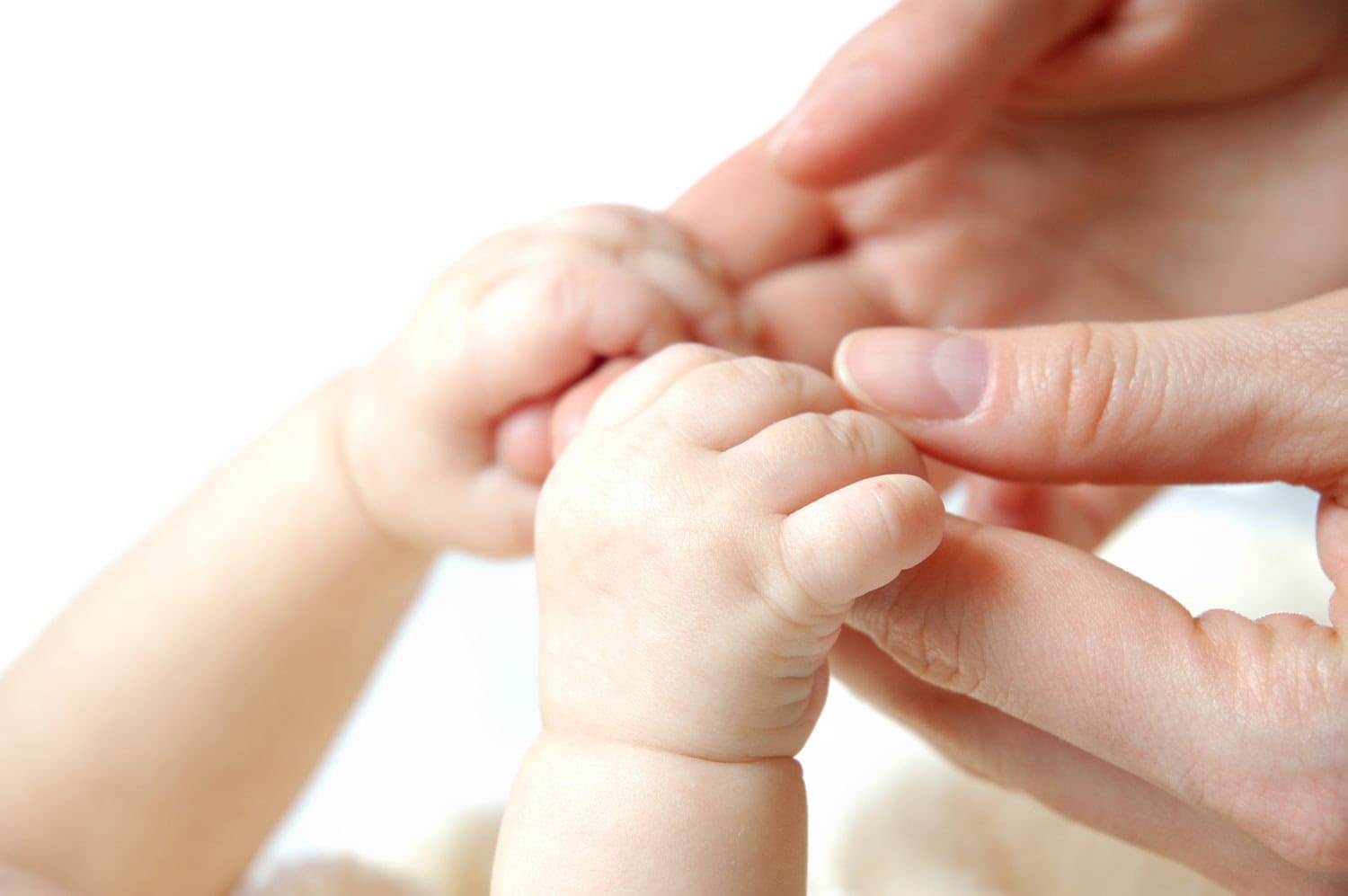 A newborn baby holding onto an to her Newborn Care Specialists fingers with a gentle grip